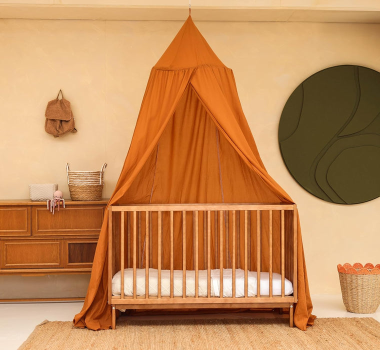 Caramel kids bed canopy hanging over crib in nursery room