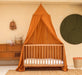Caramel kids bed canopy hanging over crib in nursery room