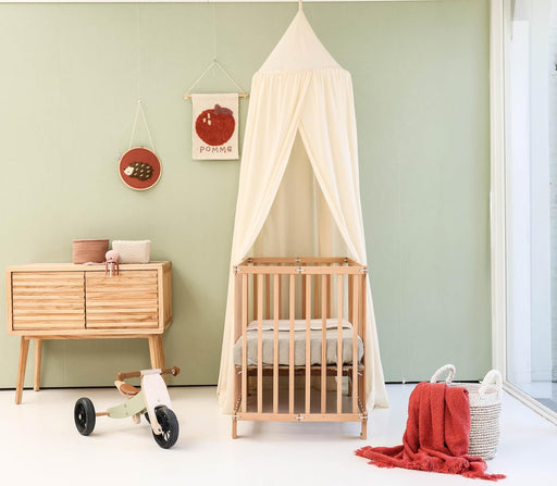 Cream beige kids bed canopy hanging over crib in nursery room
