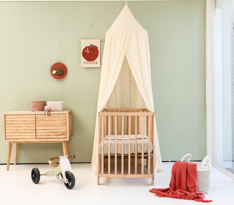 Cream beige kids bed canopy hanging over crib in nursery room